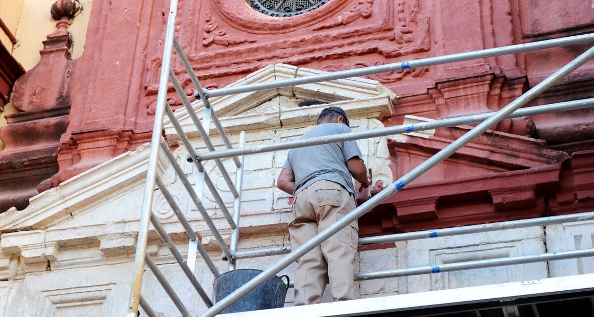 Denkmalpflege, Restaurierung. Mann auf Gerüst restauriert Fassade einer Kirche.